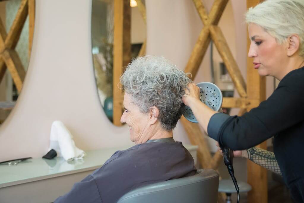 A hairdresser styling an elderly woman's hair in a salon, showcasing senior hair care.