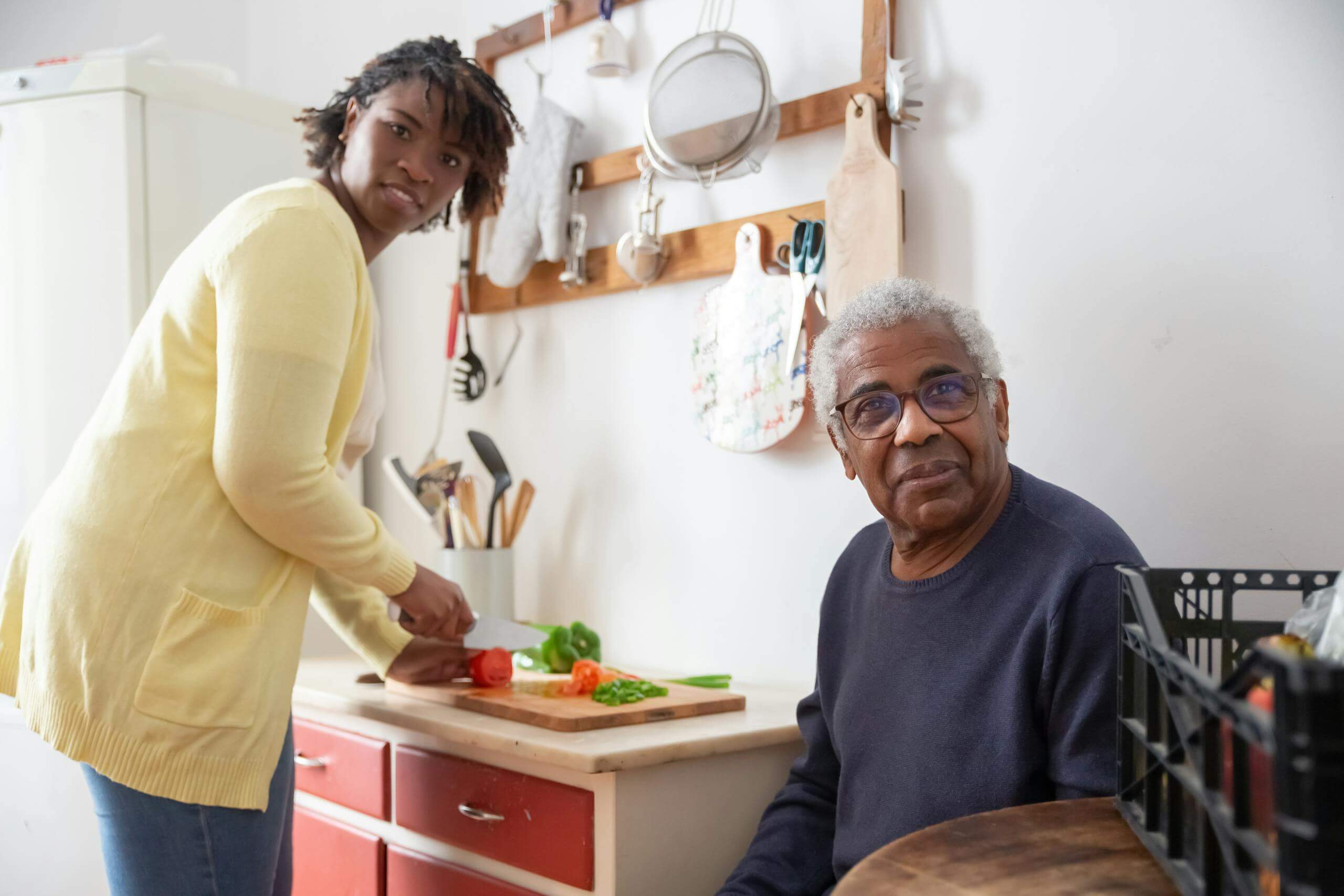 Elderly man and adult woman cooking together in a cozy kitchen setting.