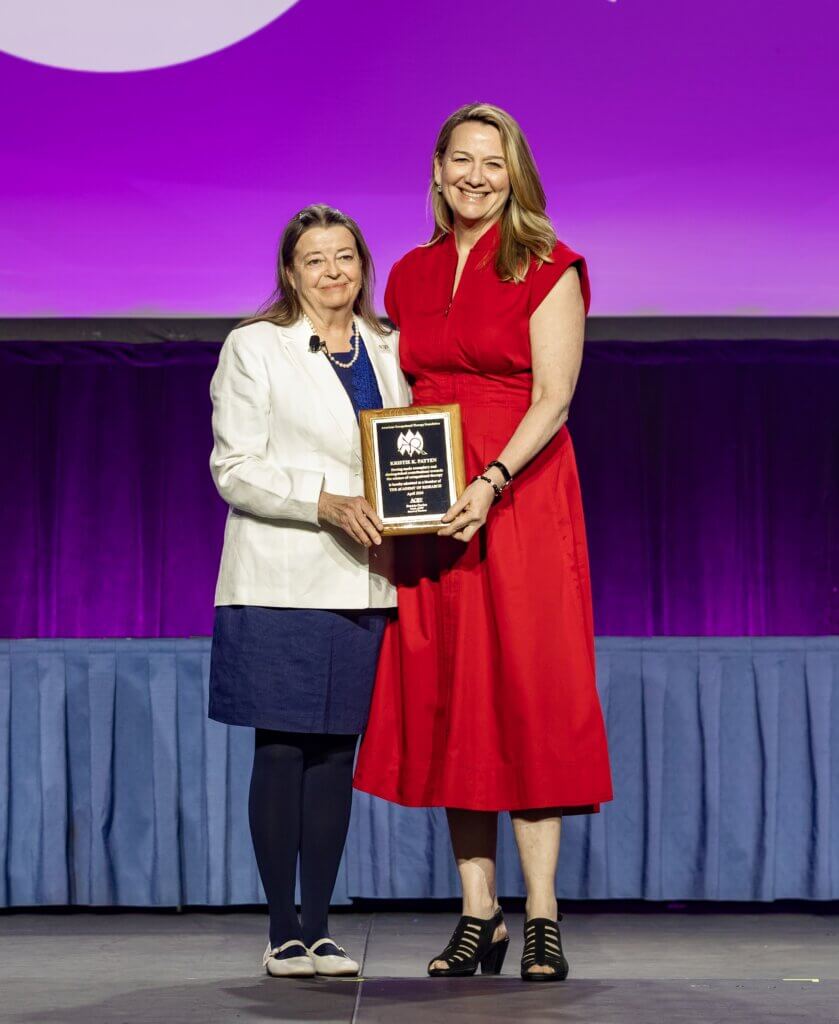A photo of our 2026 Academy of Research Nominee Kristie Patten being presented an award by our Board Chair Patti Davies on the AOTA conference stage with a purple backdrop in the background